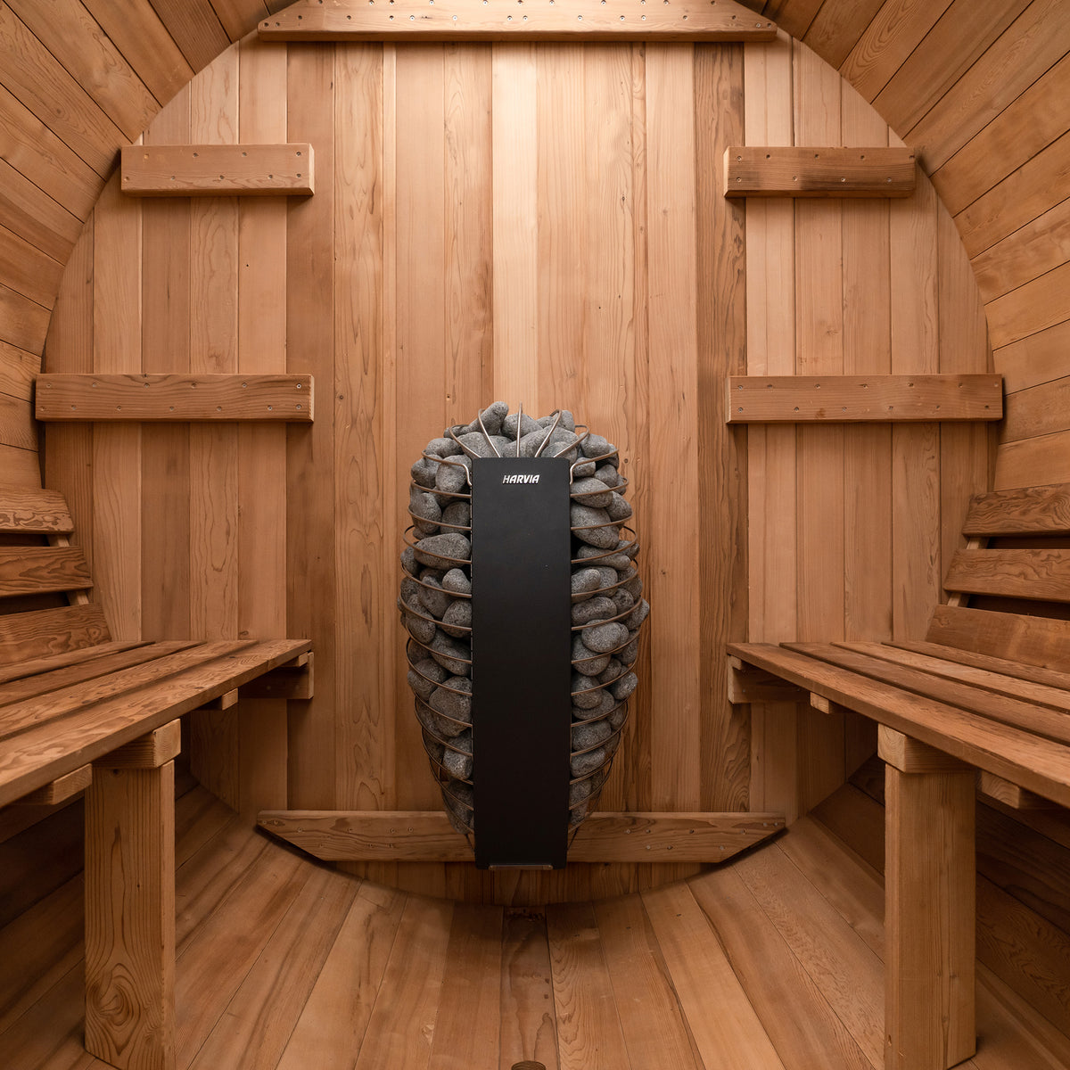 Redwood Outdoors 6 person Barrel Outdoor Sauna with porch made of hemlock, inside view from the front, two benches on either side with a heater in the rear.
