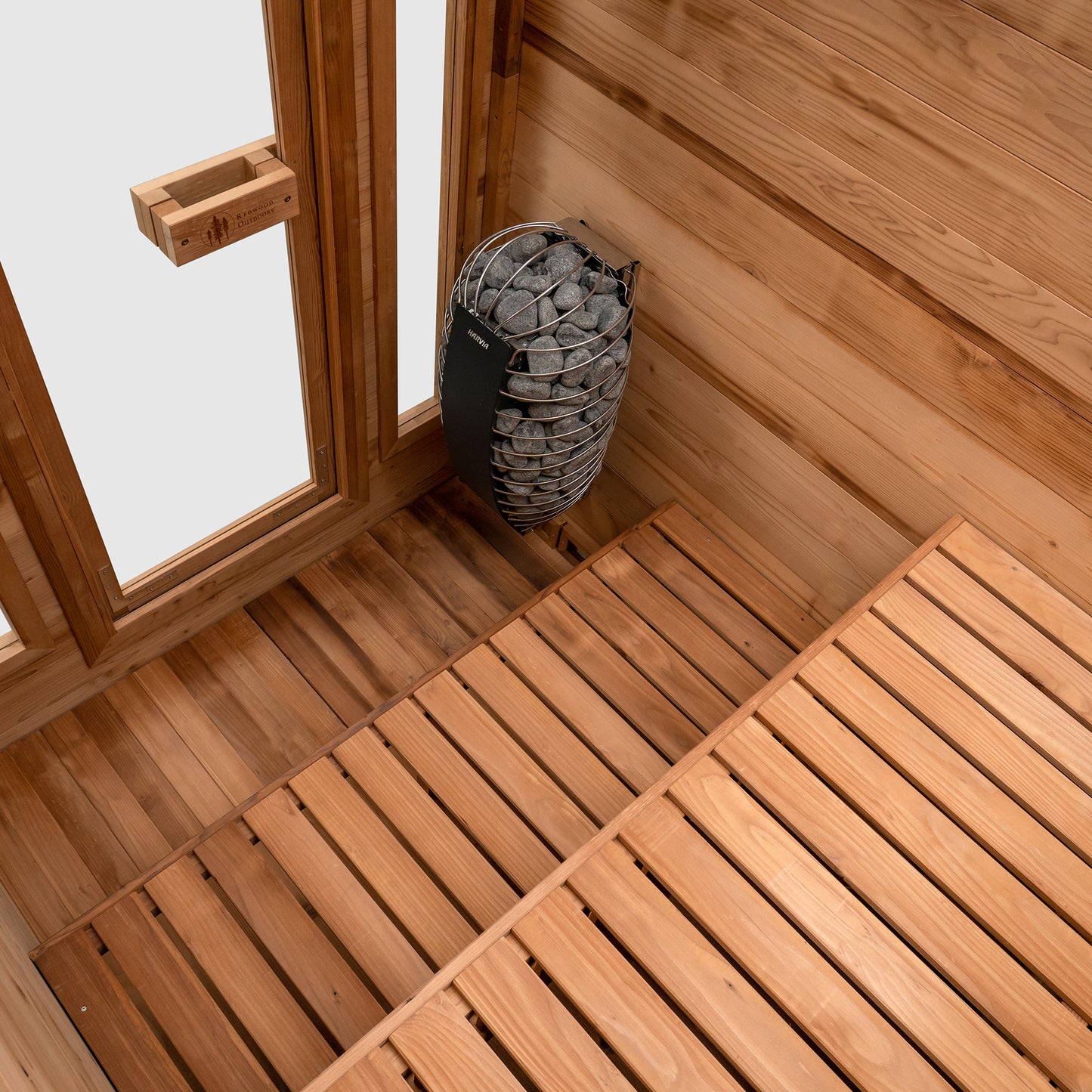 Redwood Outdoors Cabin 4 person sauna made of Hemlock wood. A front view of the inside of the sauna with duel wooden benches and a heater in the corner.
