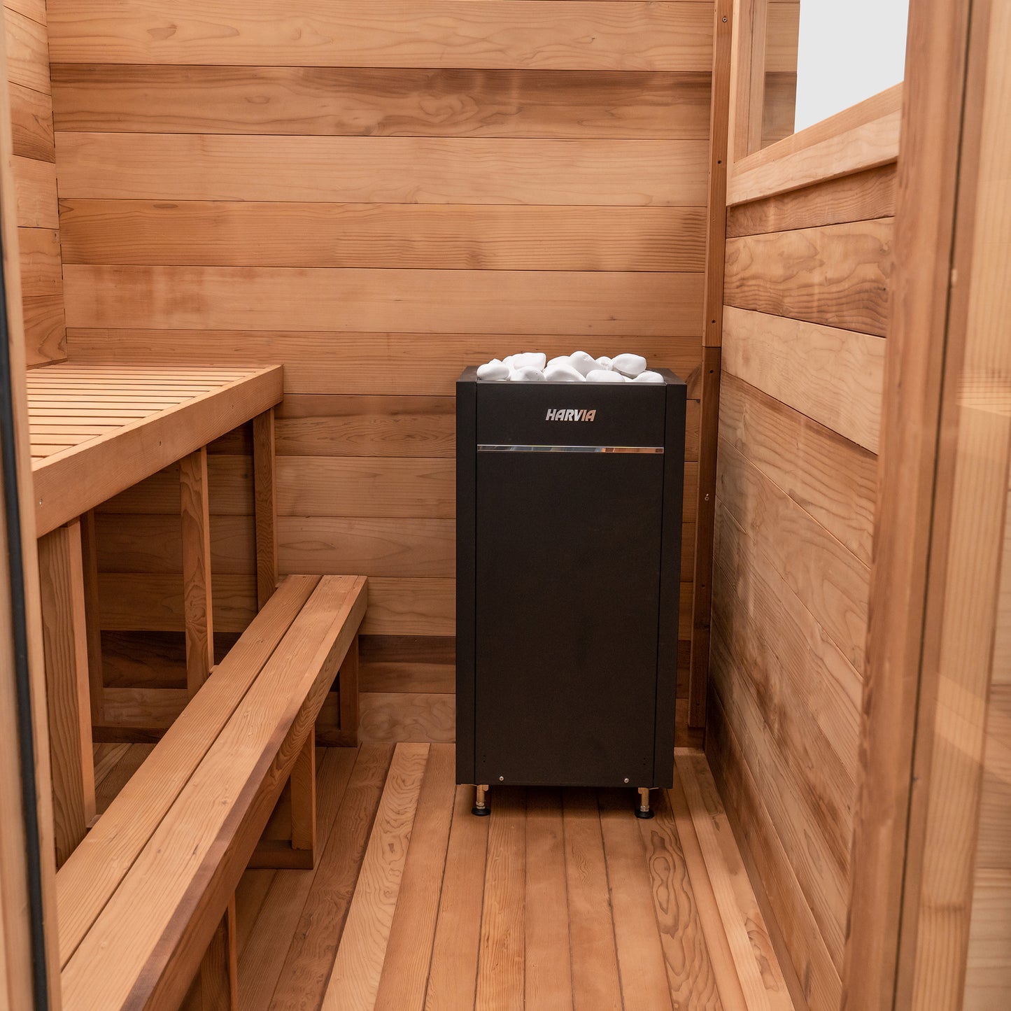 Redwood Outdoors Cove 3 person sauna made of Hemlock wood. A front view of the inside of the sauna with the wooden bench, foot rest and a heater in the corner.
