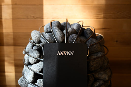 Rounded olivine diabase stones stacked loosely in a Harvia electric sauna heater, showing air gaps between the stones for proper airflow.