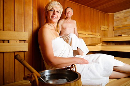 A woman and a man relaxing on the benches of a wood-lined sauna, wrapped in towels