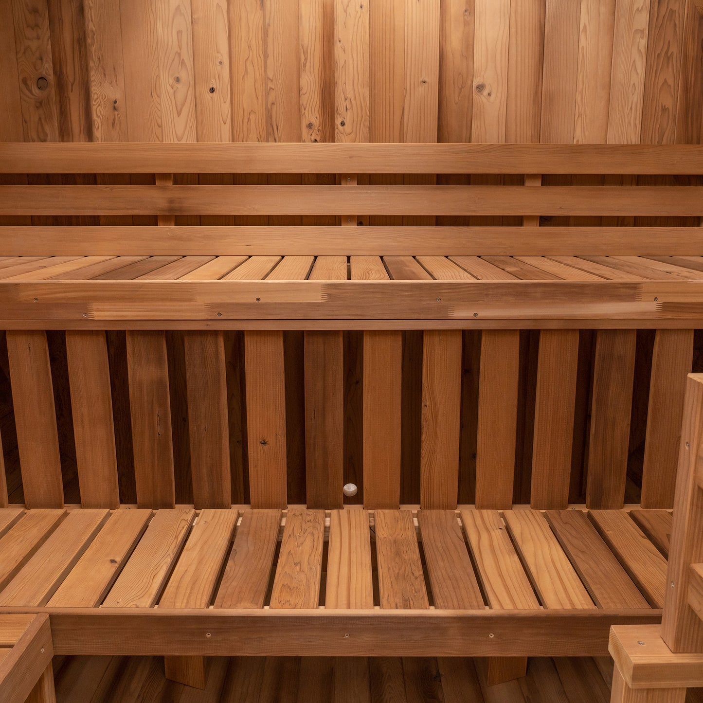 Redwood Outdoors 6 person Barrel Outdoor Extra-Wide Sauna with porch made of hemlock, inside view from the front of the sauna of two benches in the rear of the sauna.