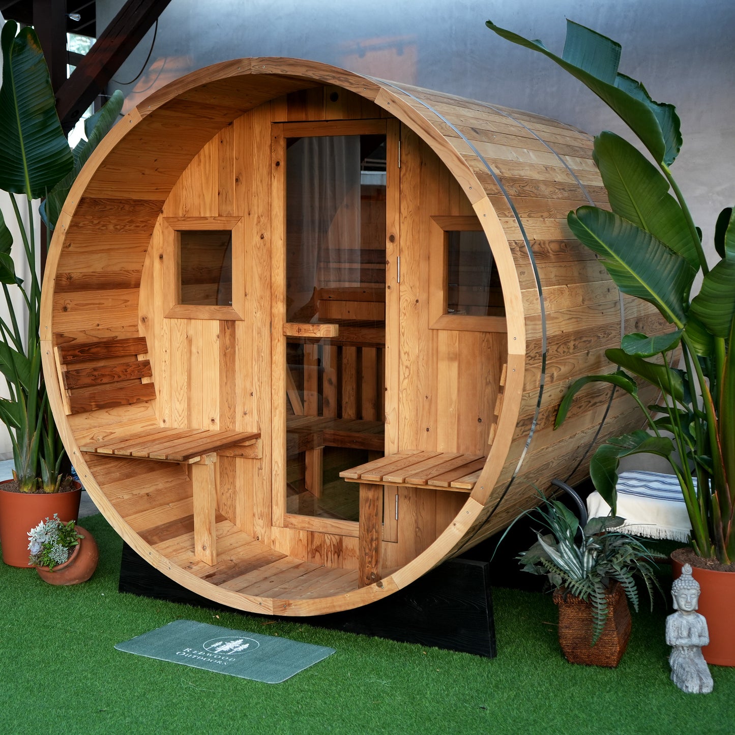 A barrel sauna with an attached porch with two seats, two windows and a full glass door. 