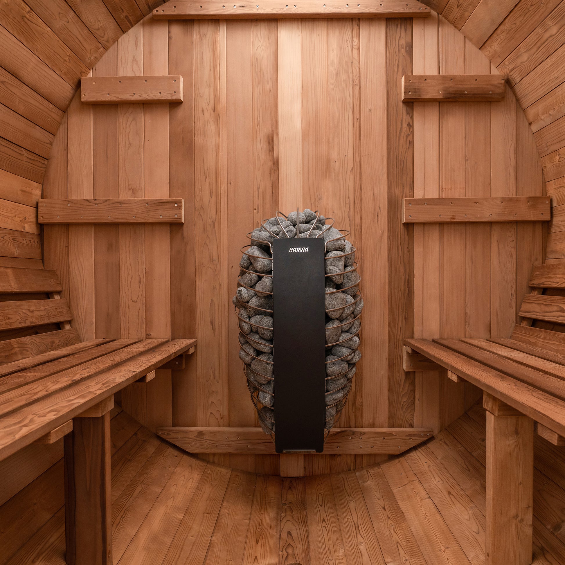 Redwood Outdoors 6 person Barrel Outdoor Sauna made of hemlock, inside view from the front, two benches on either side with a heater in the rear.