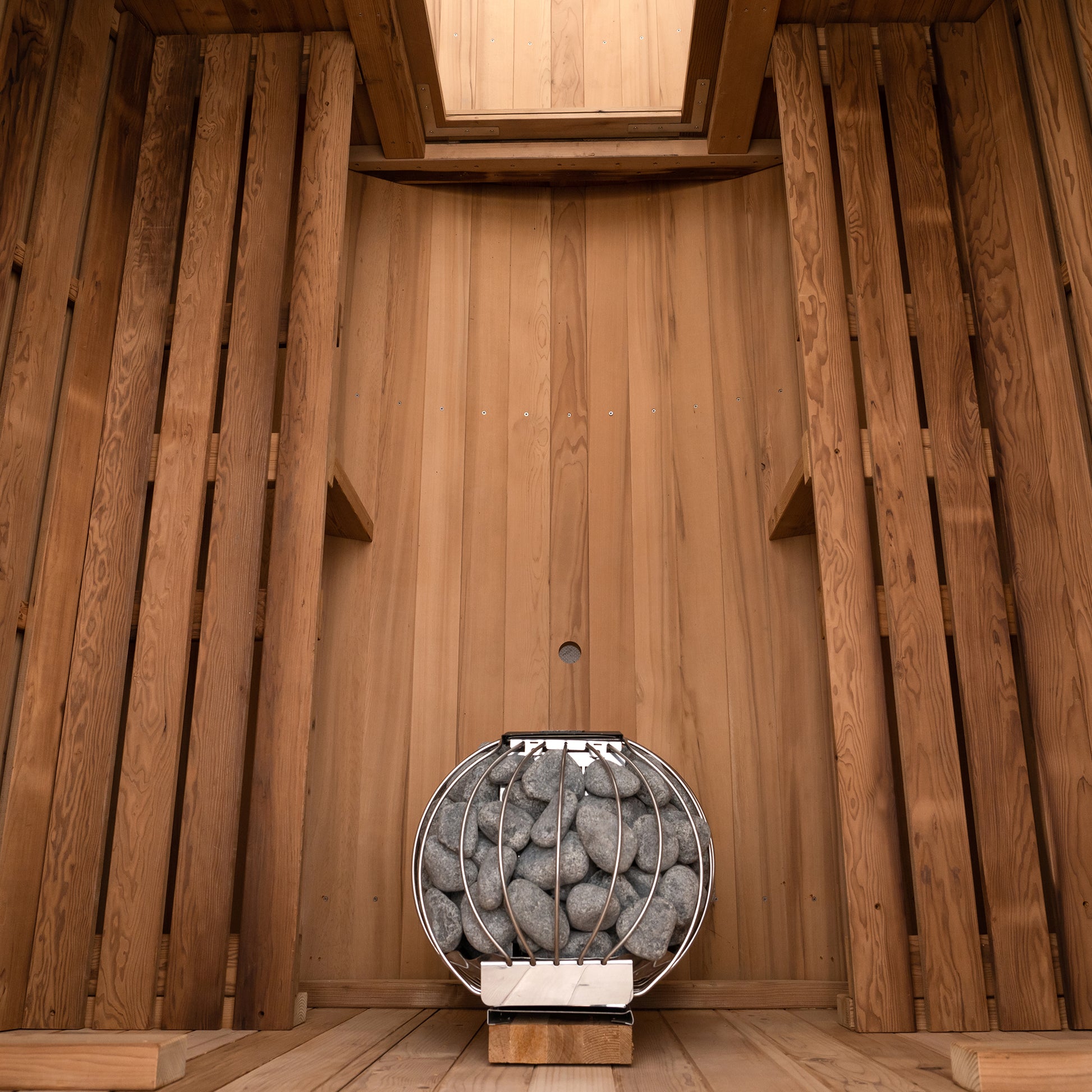 Redwood Outdoors 6 person Barrel Outdoor Sauna with porch made of hemlock, inside view from the front, two benches on either side with a heater in the rear.