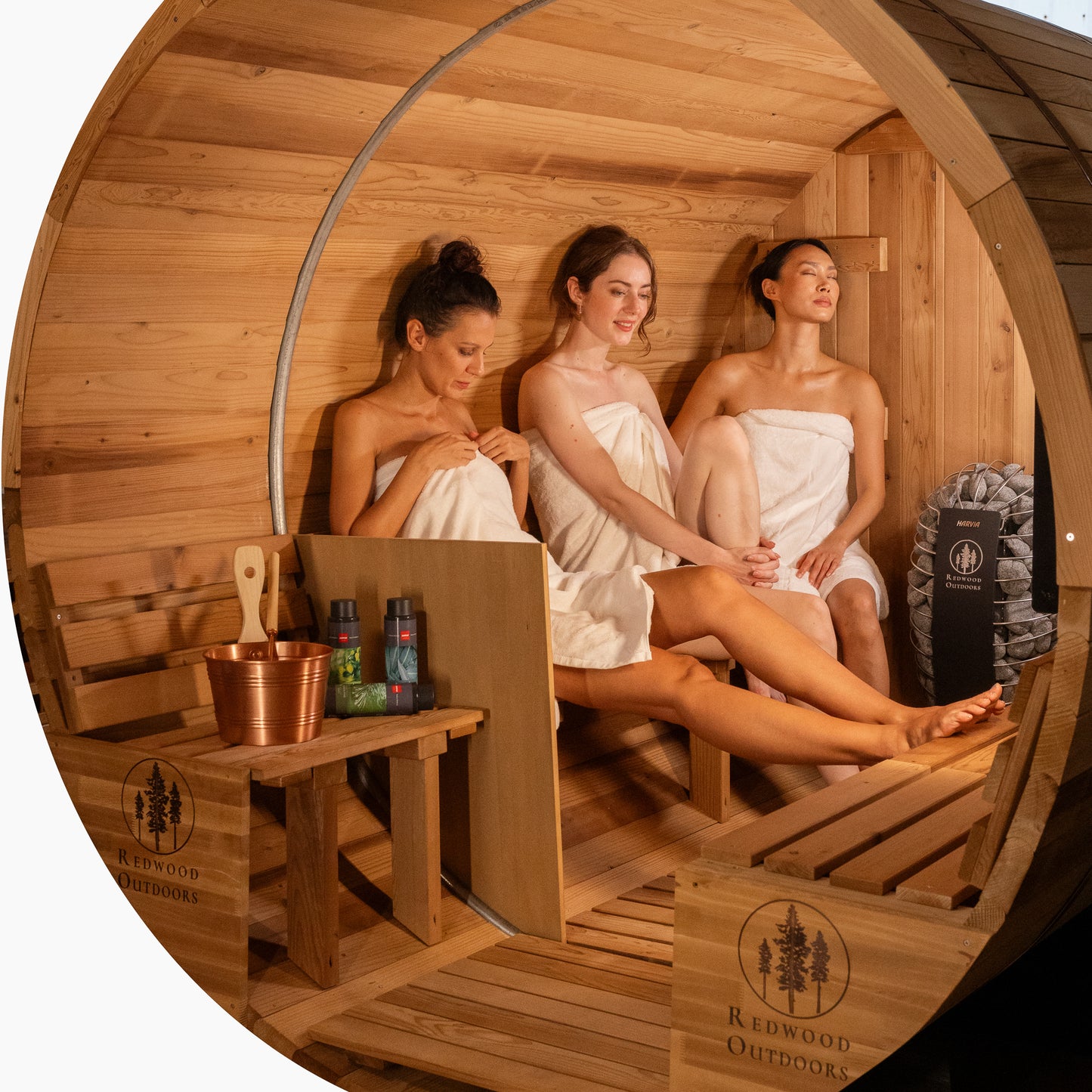 Redwood Outdoors 6 person Barrel Outdoor Sauna with porch made of hemlock, inside view of three people sitting on a bench of the sauna.