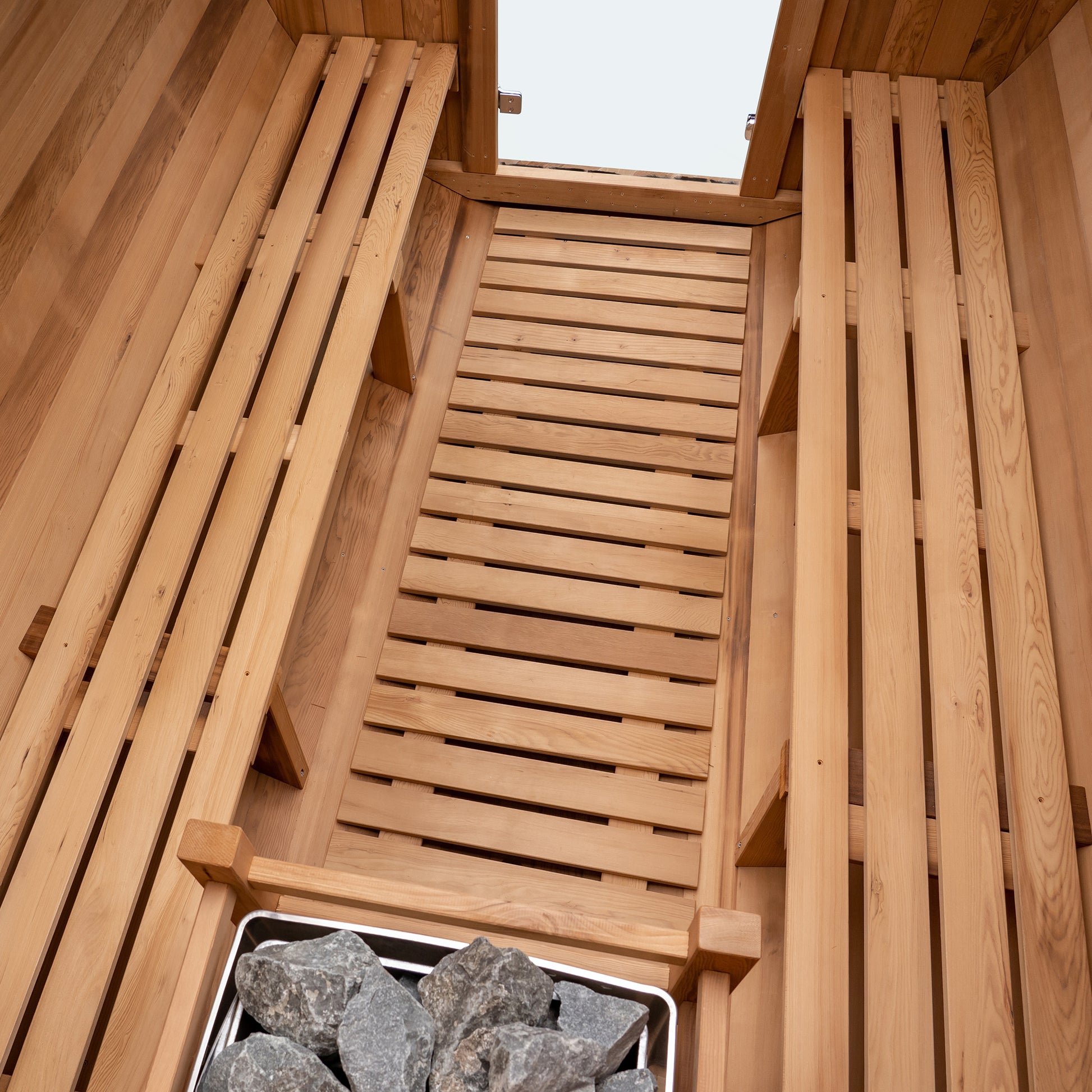 Redwood Outdoors 8 person Barrel Outdoor Sauna made of hemlock, inside view from above, two benches on either side with a heater in the rear.