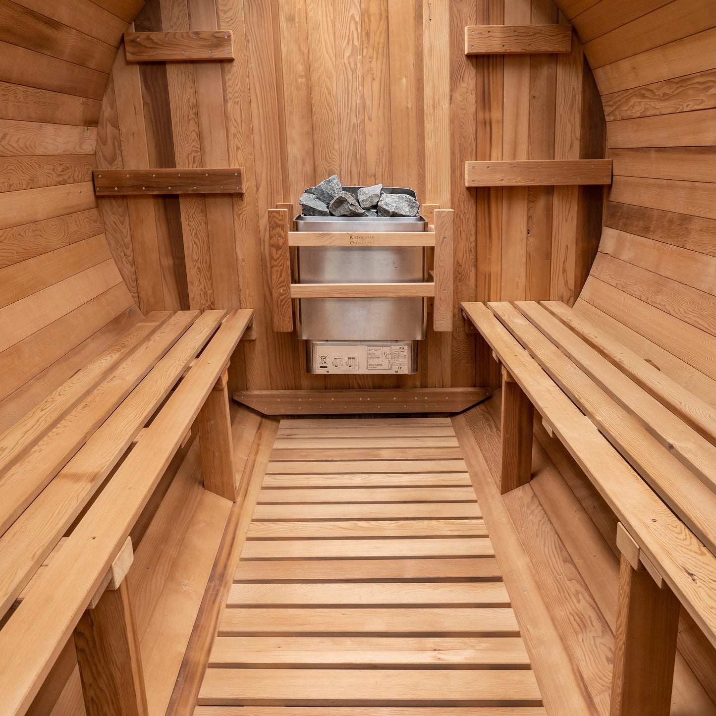 Redwood Outdoors 8 person Barrel Outdoor Sauna made of hemlock, inside view from the front, two benches on either side with a heater in the rear.
