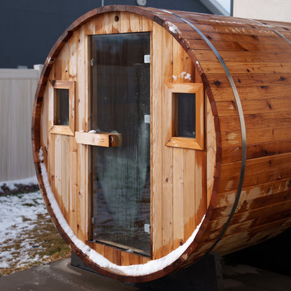 Redwood Outdoors 8 person Barrel Outdoor Sauna made of hemlock with a glass door and two windows, front outside lifestyle view in the snow. 