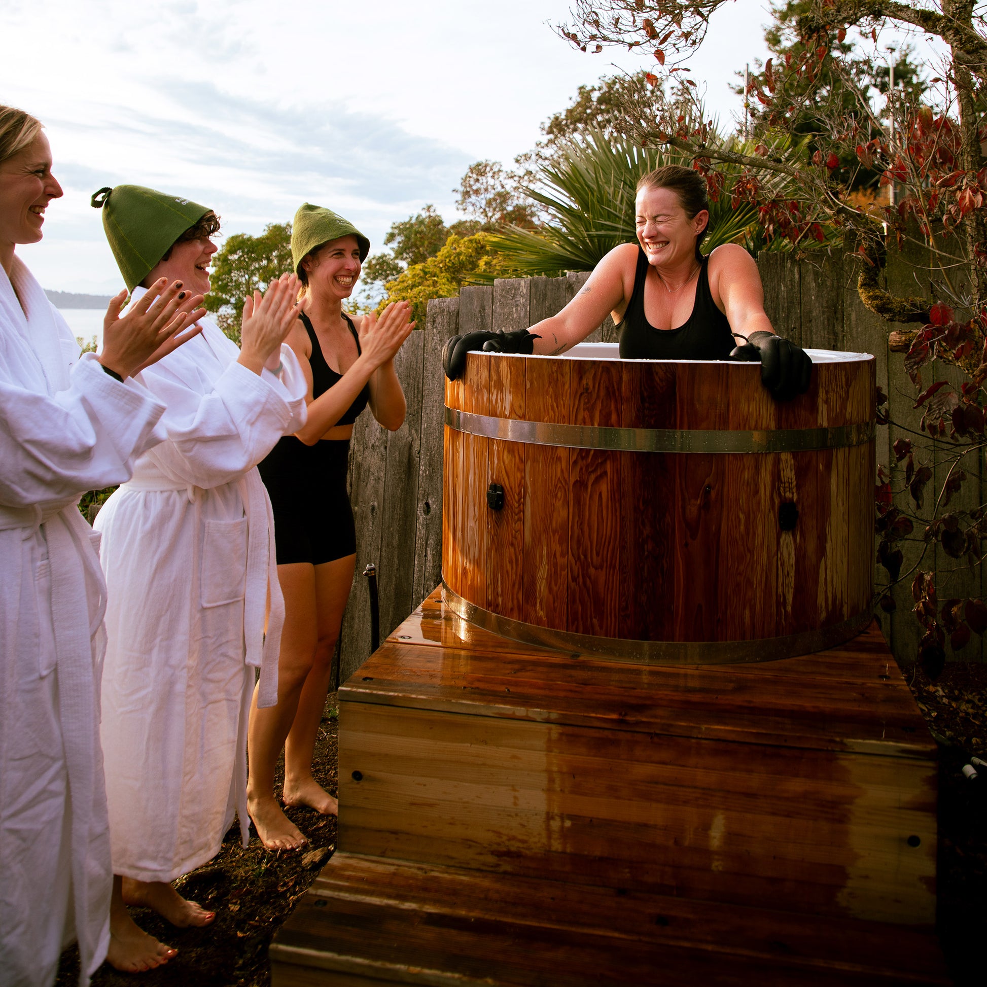 Redwood Outdoors Alaskan All-In_One Cold Plunge Tub made of heat treated wood exterior lifestyle view with a person in the tub with three other people outside of the tub.