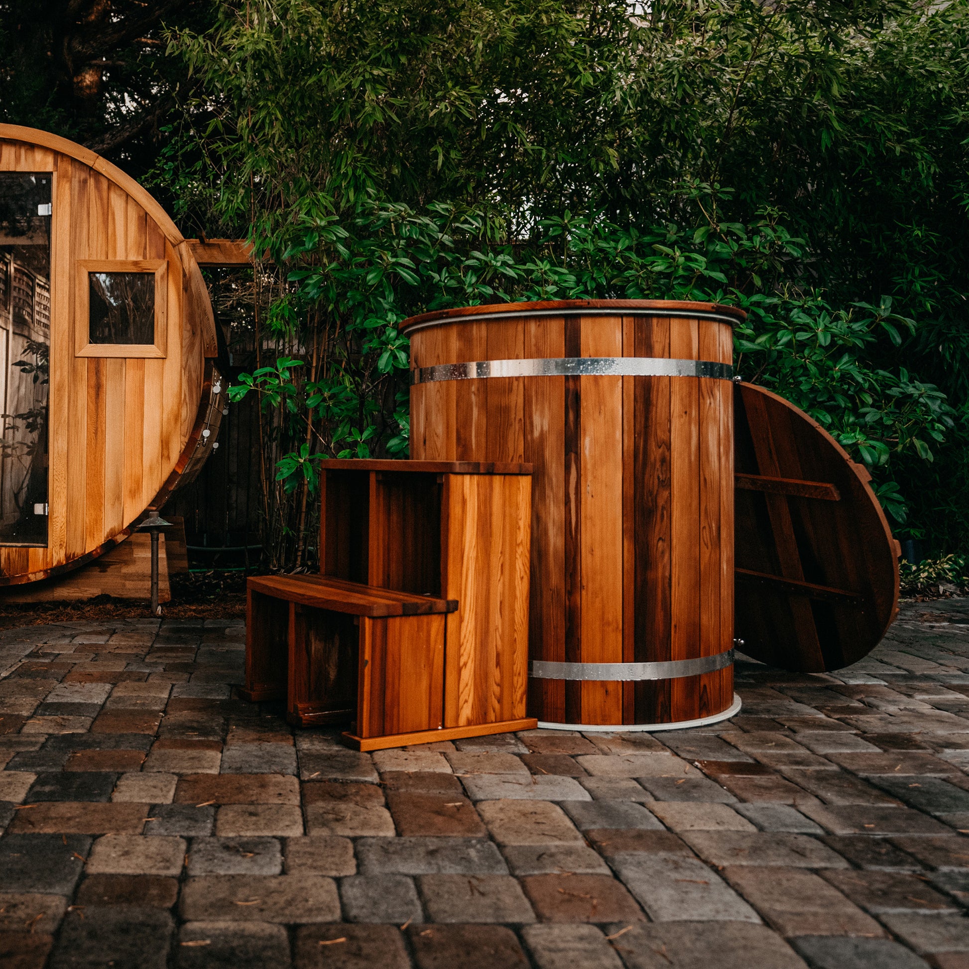 Redwood Outdoors Alaskan Cold Plunge Tub made of heat treated wood exterior view with the lid off and stairs on a patio made of pavers. 