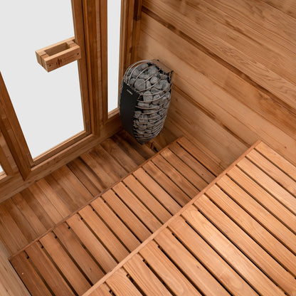 Redwood Outdoors Cabin 4 person sauna made of Hemlock wood. A front view of the inside of the sauna with duel wooden benches and a heater in the corner.