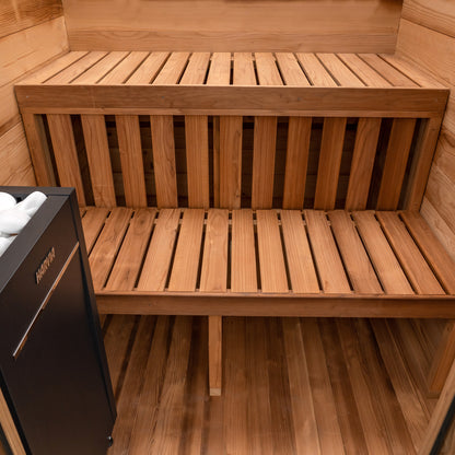 Redwood Outdoors Cabin 4 person sauna made of Hemlock wood. A front view of the inside of the sauna with duel wooden benches and a heater in the corner.