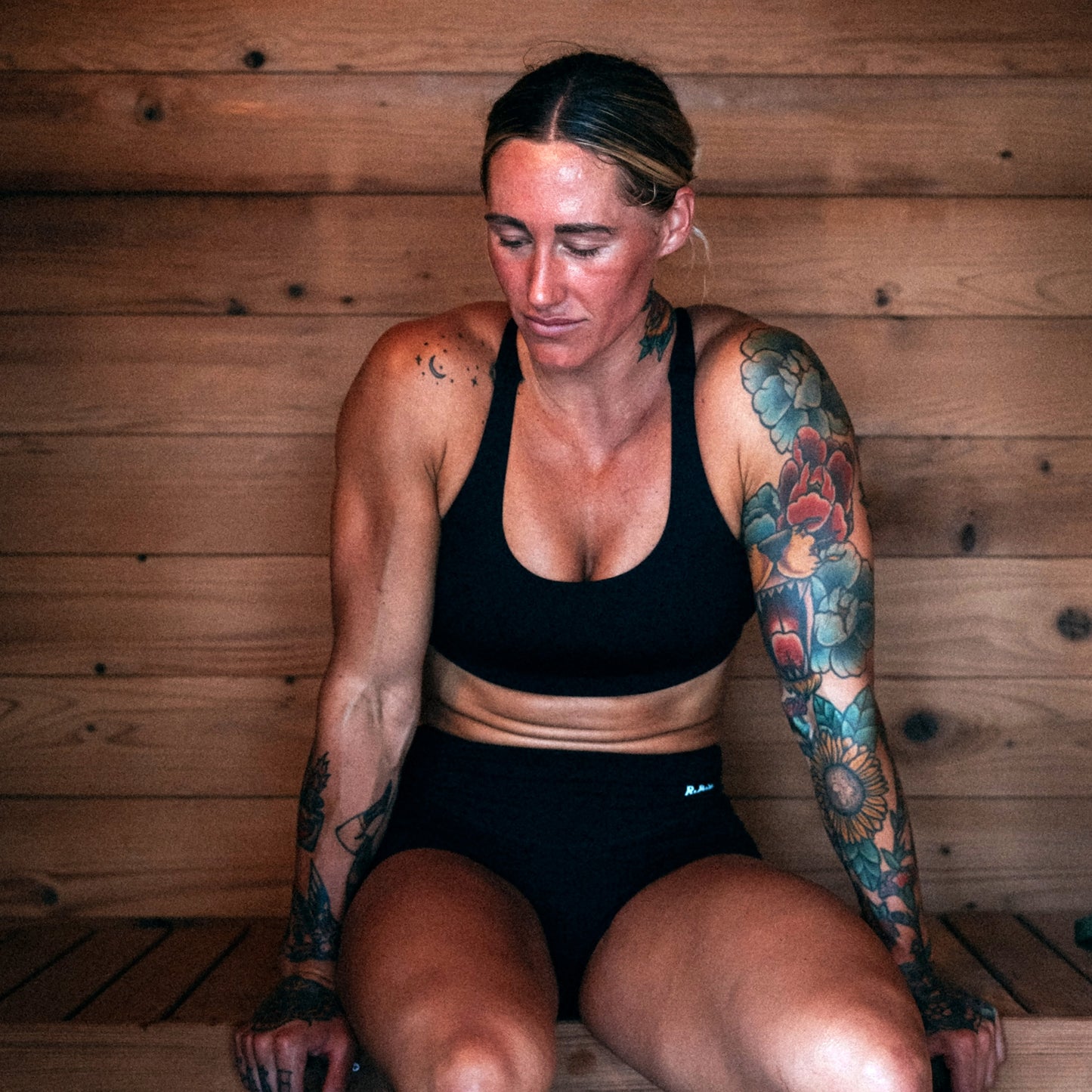 Redwood Outdoors Cabin 4 person outdoor sauna made of hemlock wood. A lifestyle view of a woman sitting inside of the sauna on a bench.