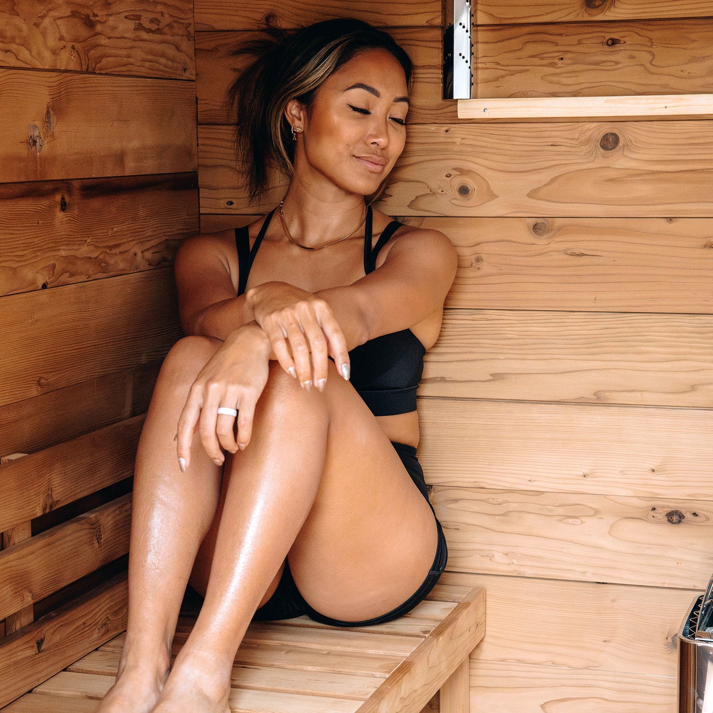 Redwood Outdoors Cove 3 person sauna, made of hemlock wood. A lifestyle view inside the sauna of a women sitting on a bench.