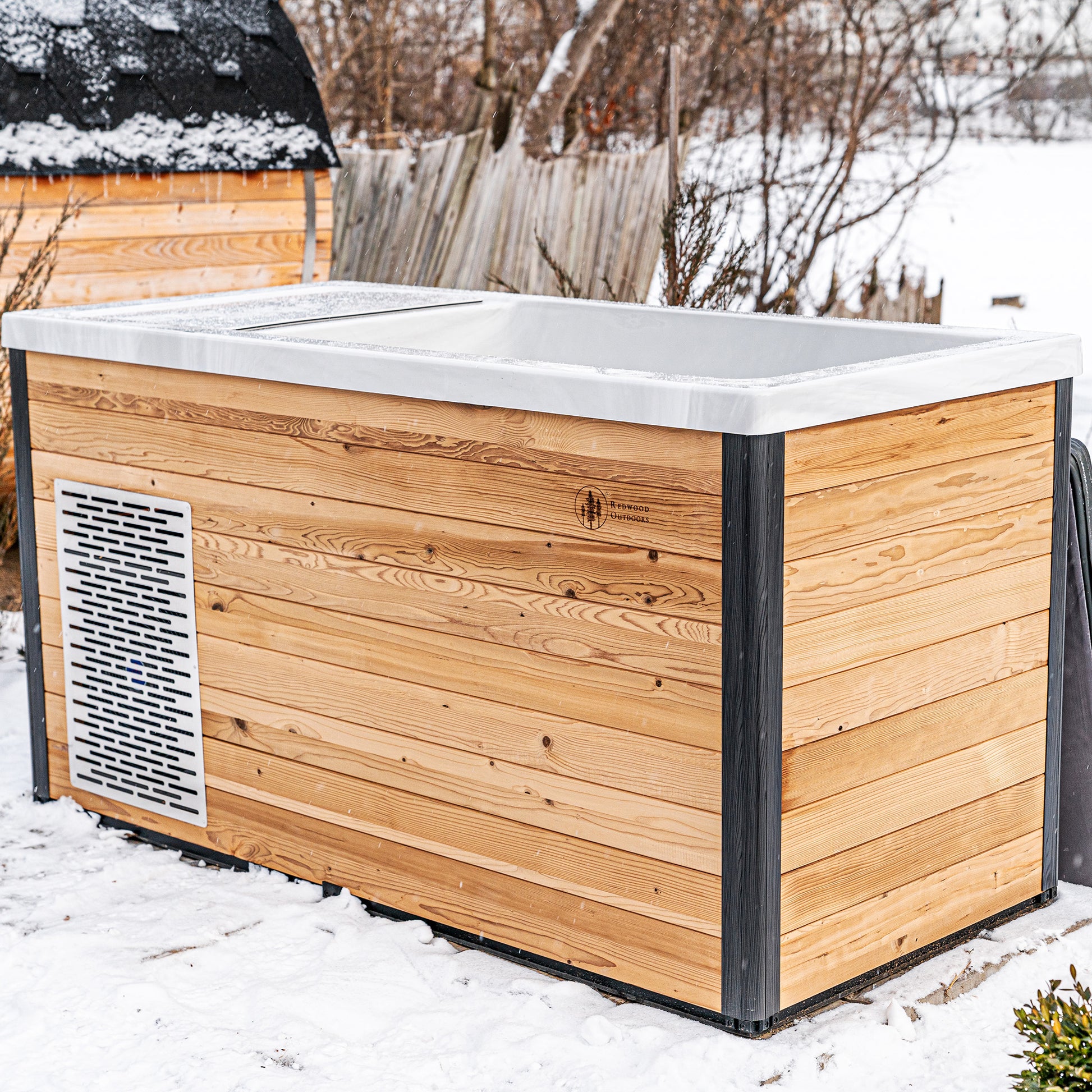 Redwood Outdoors Denali All-In_One Cold Plunge Tub made of heat treated wood exterior life style view with the lid off in the snow