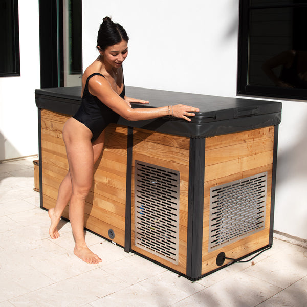 Redwood Outdoors Denali All-In_One Cold Plunge Tub made of heat treated wood exterior lifestyle view with the lid on and a person standing next to the cold plunge