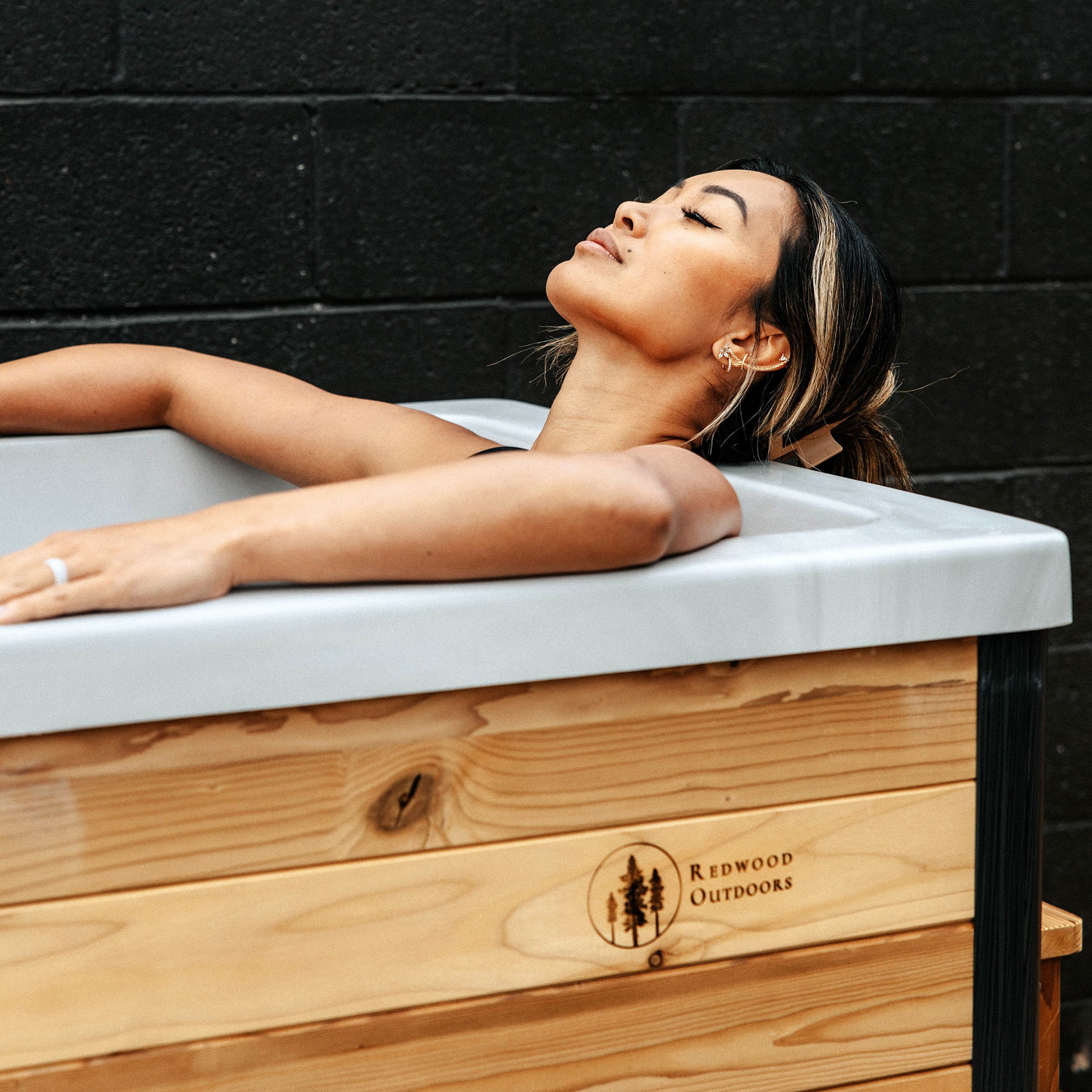 Redwood Outdoors Denali All-In_One Cold Plunge Tub made of heat treated wood exterior lifestyle view with a person in the tub.