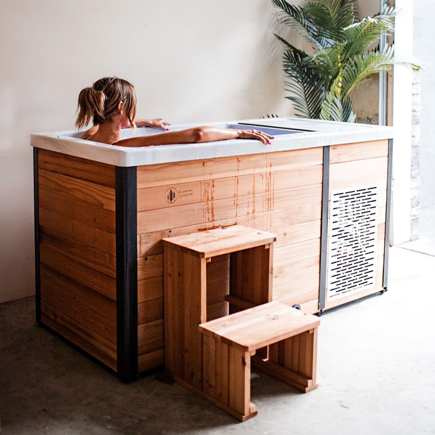Redwood Outdoors Denali All-In_One Cold Plunge Tub made of heat treated wood exterior lifestyle view of a person sitting in the cold plunge in a indoor setting.