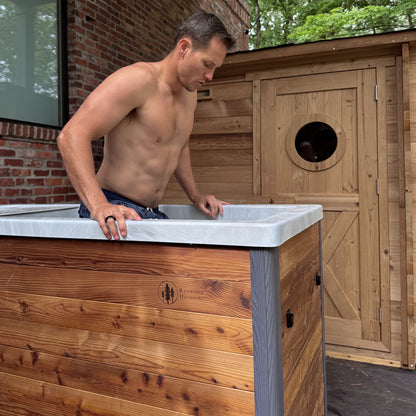 Redwood Outdoors Denali All-In_One Cold Plunge Tub made of heat treated wood exterior lifestyle view with the lid off and a person getting into the cold plunge.