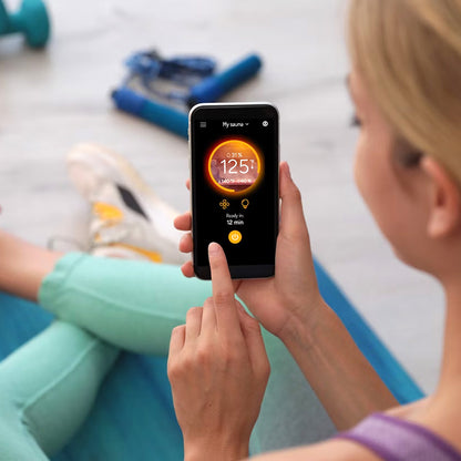 View of the MyHarvia 2 app being shown on a smart phone displaying the saunas temperature while a person is in a gym.