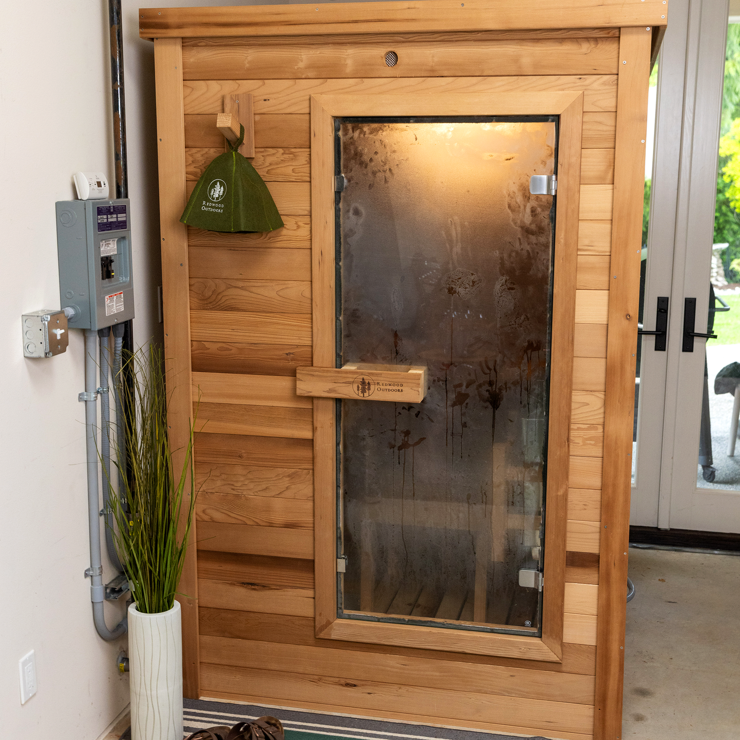Redwood Outdoors Haven 3 person indoor sauna, made of hemlock wood with a glass door exterior lifestyle view with steam on door  