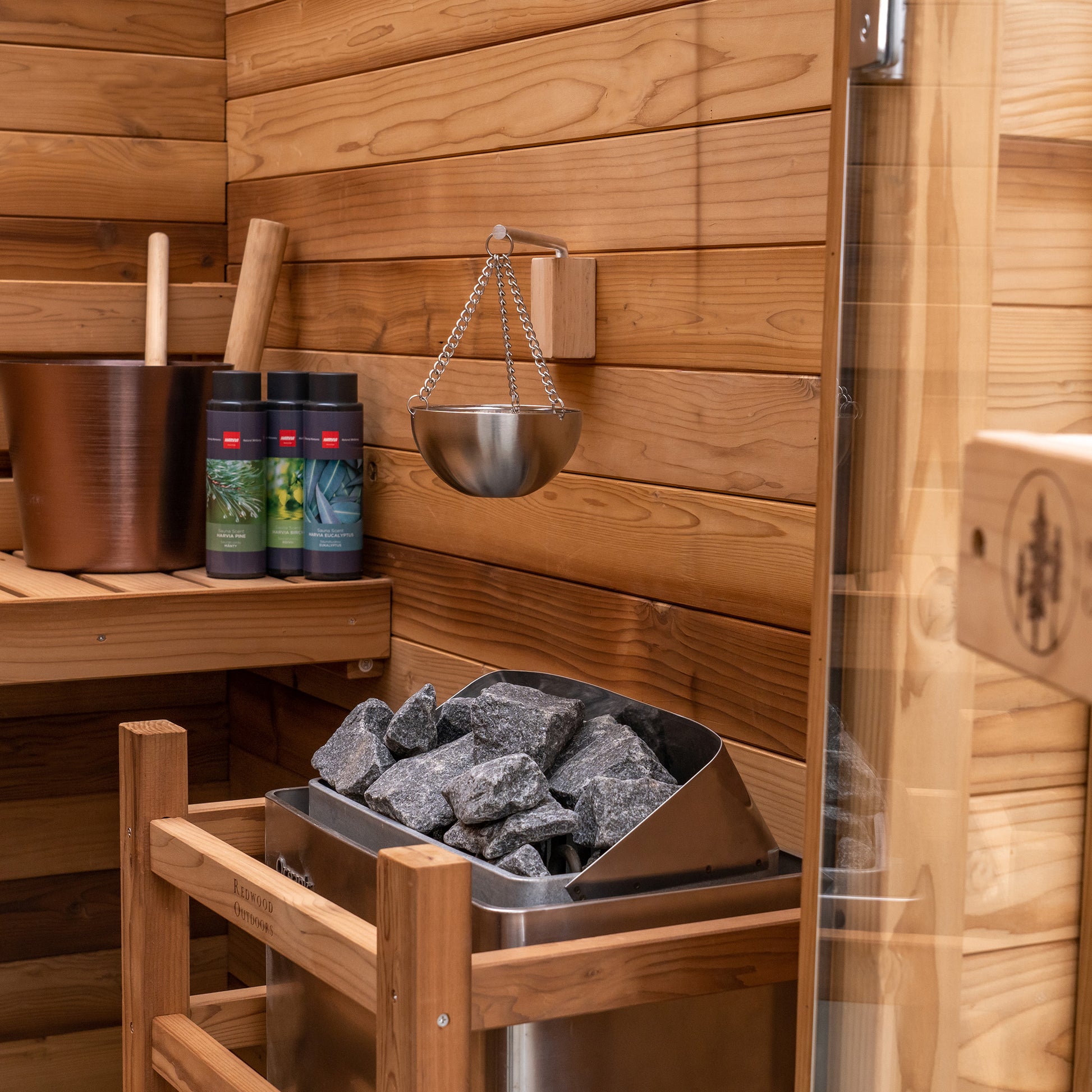 Redwood Outdoors Haven 3 person indoor sauna, made of hemlock wood with a glass door interior lifestyle view of heater and accessories