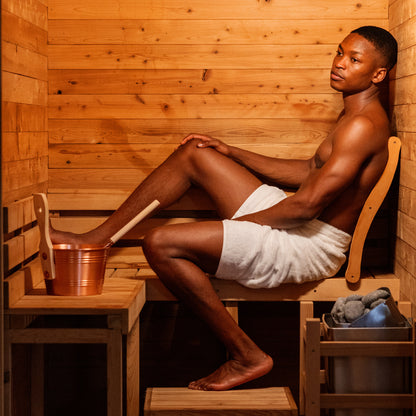 Redwood Outdoors Haven 3 person indoor sauna, made of hemlock wood interior lifestyle view of a person sitting in the sauna 