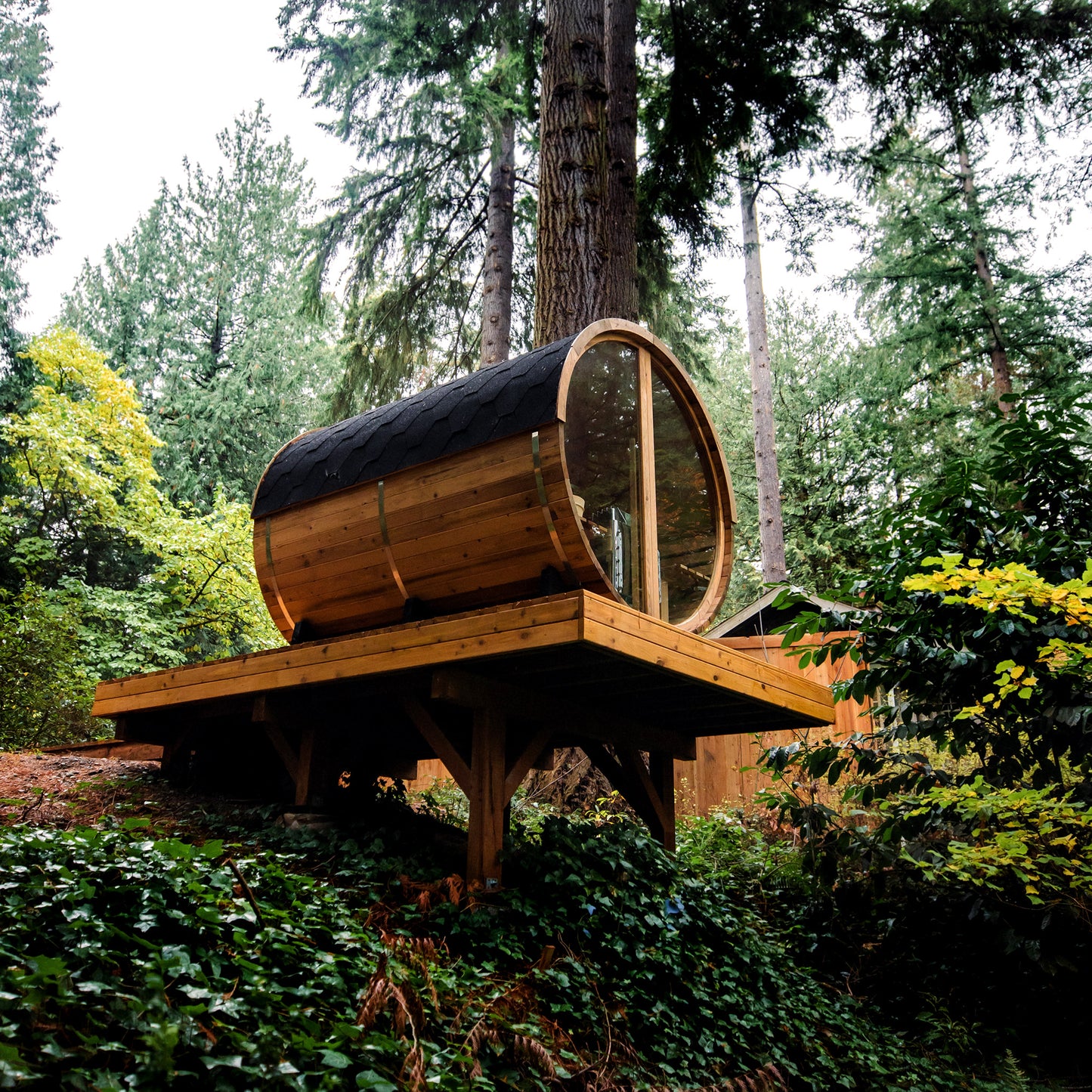 Redwood Outdoors Horizon 6 person outdoor sauna with porch rear view of the sauna on a deck overlooking an outdoor space in the daylight.  