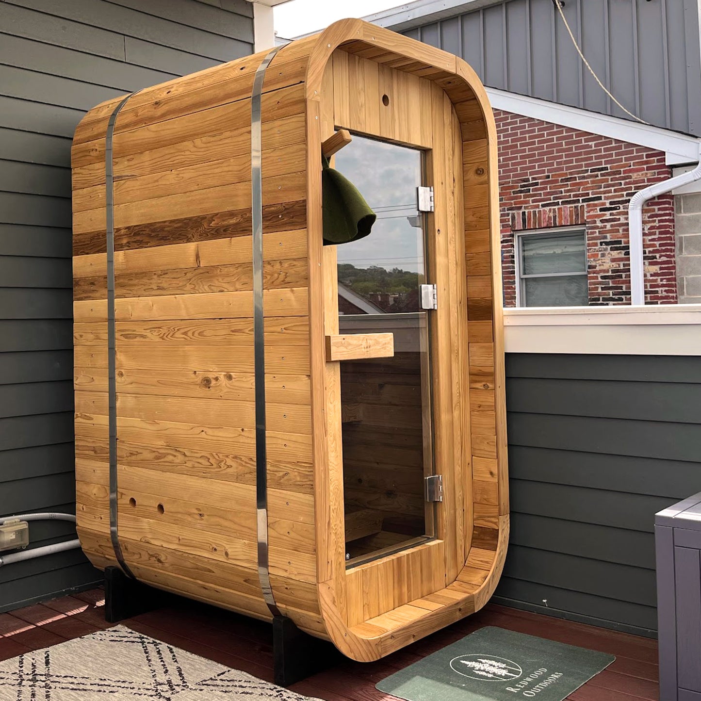 Redwood Outdoors Solo 1 person outdoor sauna, made of hemlock wood with a glass door on a balcony in the city.