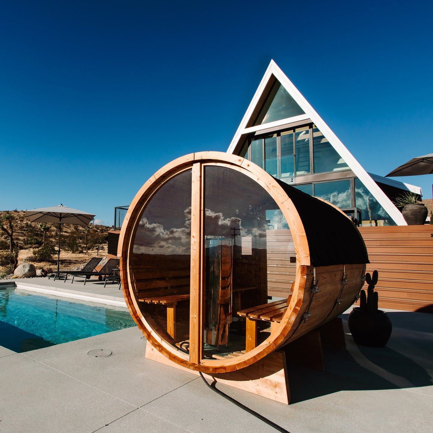 Redwood Outdoors Vista 6 person outdoor sauna, made of hemlock wood with glass door and large rear window, view from a rear side angle with a dessert in the background. 