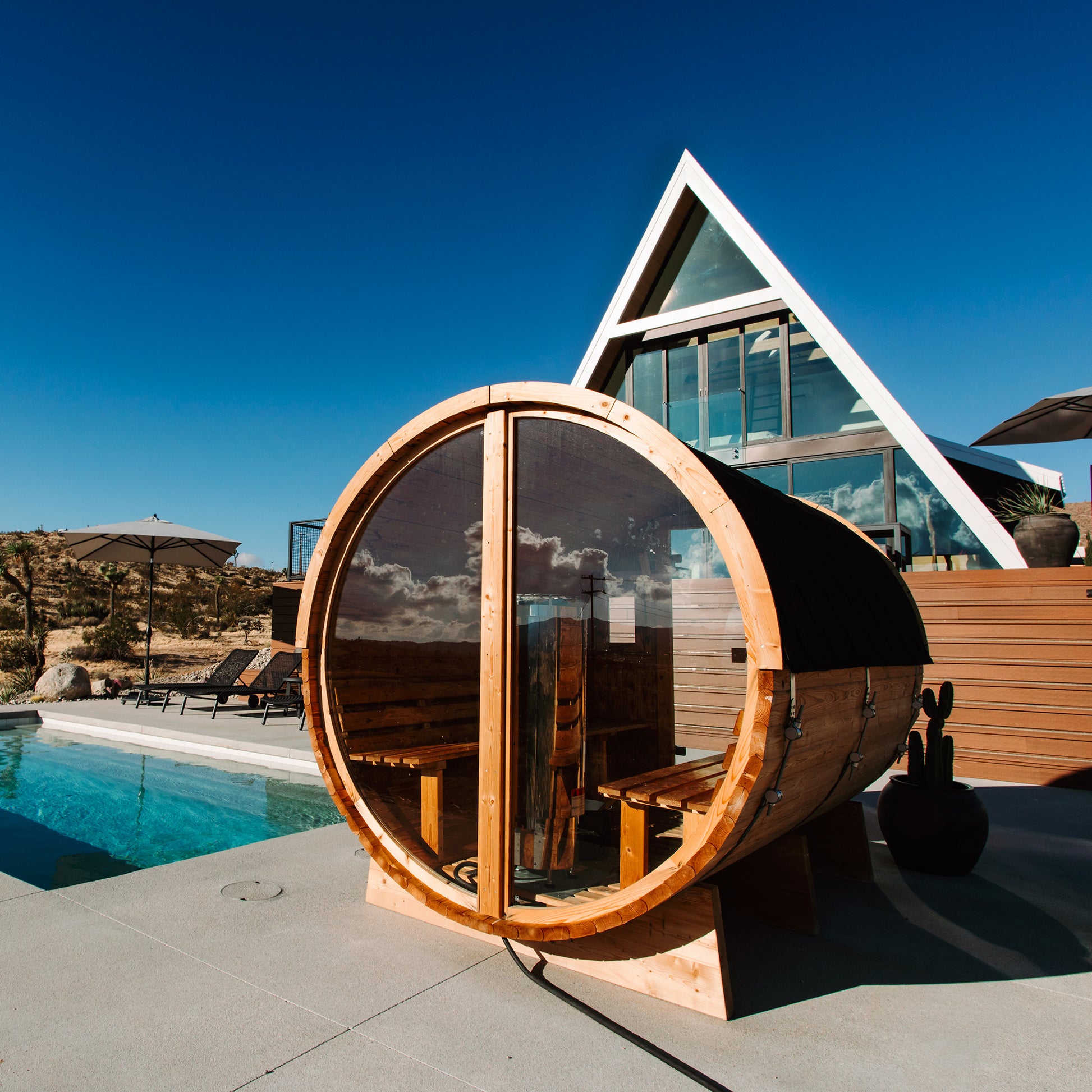 Redwood Outdoors Vista 6 person outdoor sauna, made of hemlock wood with glass door and large rear window, view from a rear side angle with a dessert in the background. 